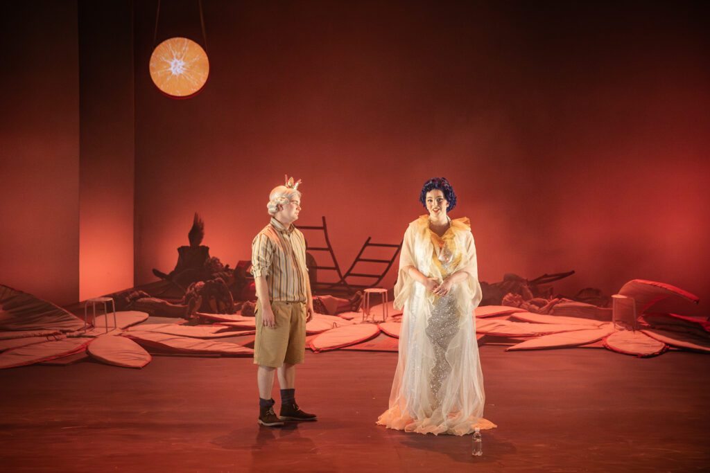 Two opera singers in costume standing on stage. The lighting is red and there is a moon in the left hand corner
