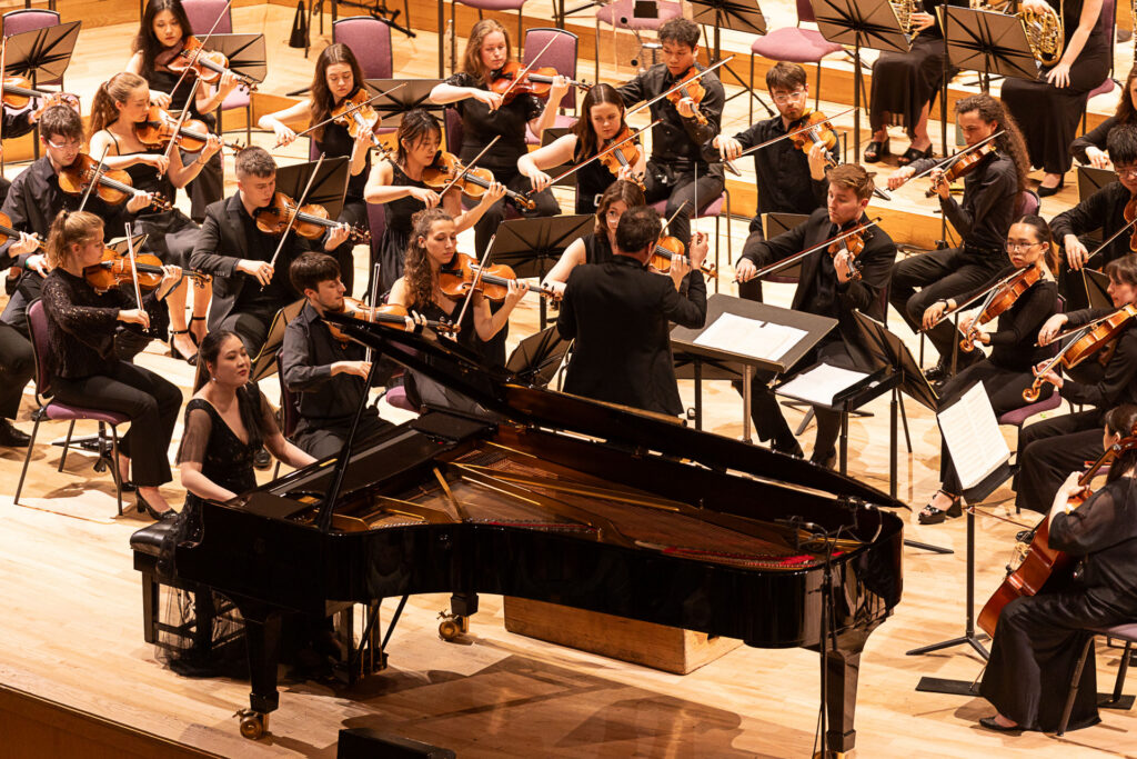 full orchestra on stage with a pianist playing a grand piano