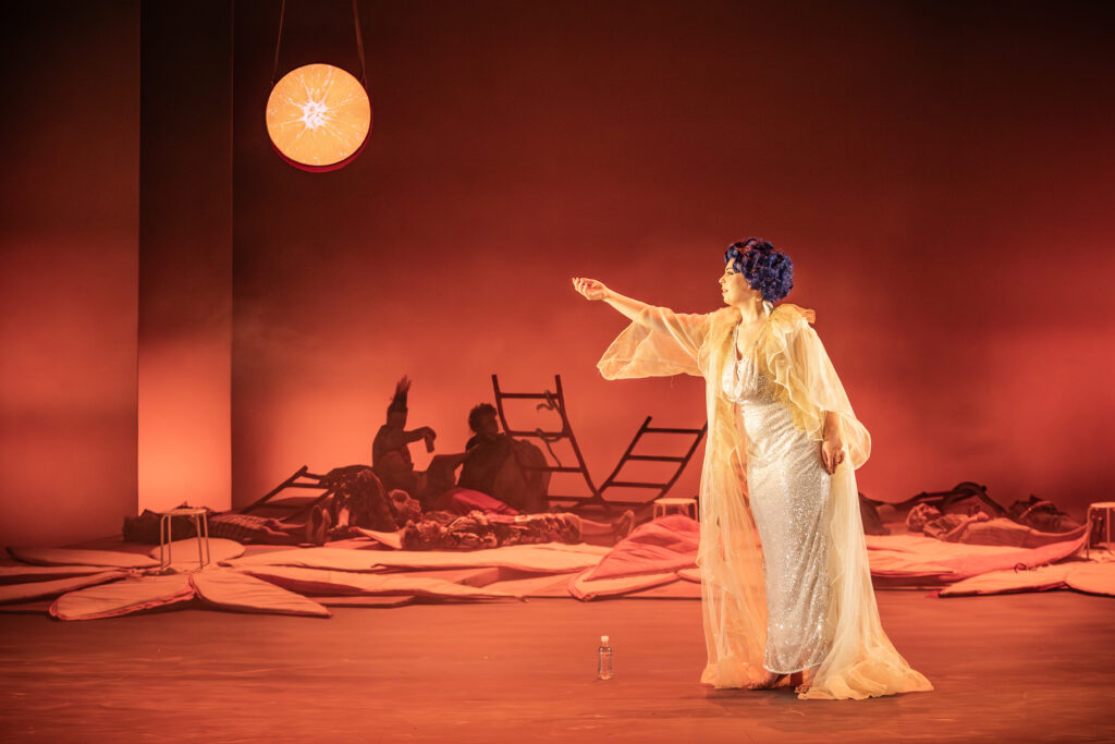 Female opera singer on stage in the moonlight. She is pointing to the left.
