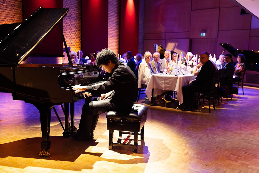 PIano soloist playing a grand piano in front of a small audience sitting at a candle-lit dinner table.